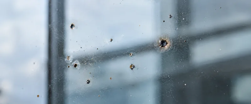 Chispa de soldadura incrustada en el vidrio, con cráteres y halo de óxido